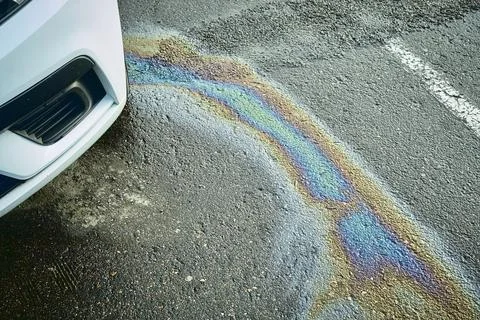 Car leaking engine oil, creating a colorful iridescent rainbow pattern on dark Stock Photos
