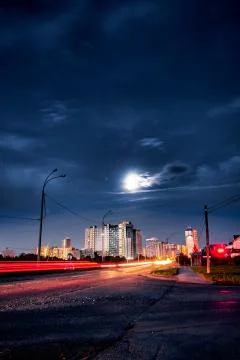 Car light trails in front of distant downtown buildings at summer night Stock Photos