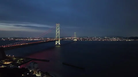 Car lights on span of long suspension bridge to city in twilight Stock Footage 242344869