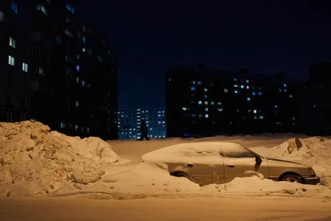 A car littered with snow stands on the side of the night city in the light lamp. 스톡 사진
