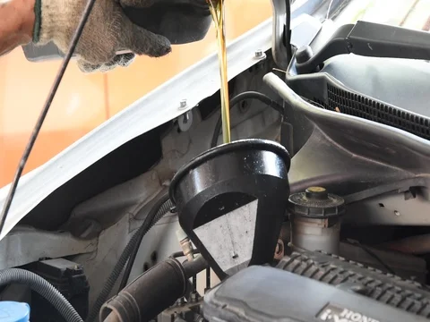 Car maintenance servicing mechanic pouring new oil lubricant into the car engine Stock Footage 77633402