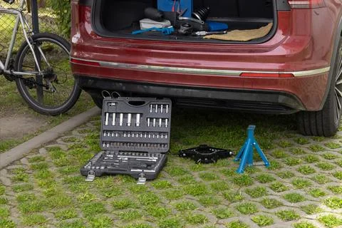 Car maintenance tools next to red car in outdoor parking area Stock Photos