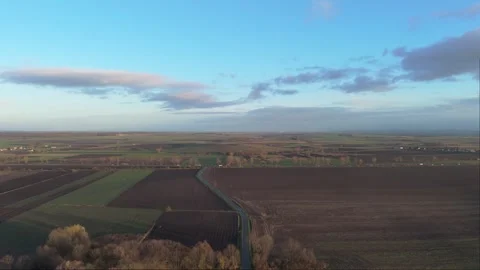 A car meanders along a road through fields, captured by a drone in the warm.. Video stock 257423152