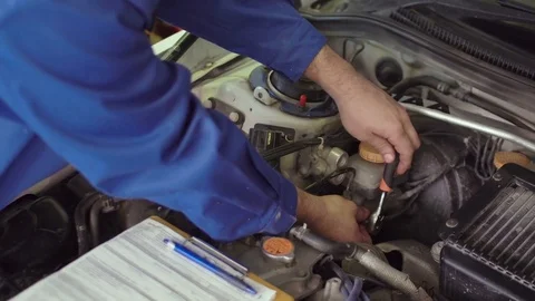 Car mechanic in a blue uniform fixing car under opened hood, diagnostics Stock Footage 74685352