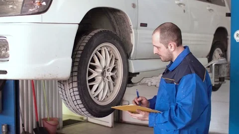 Car mechanic is checking breaks and writing in notepad on lifted white car Video stock 74898527