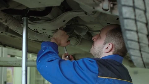 Car mechanic is checking car suspension on lifted crossover car in blue overalls Video stock 74858261