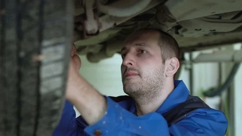 Car mechanic is checking car suspension on lifted crossover car in blue overalls Video stock 74861570