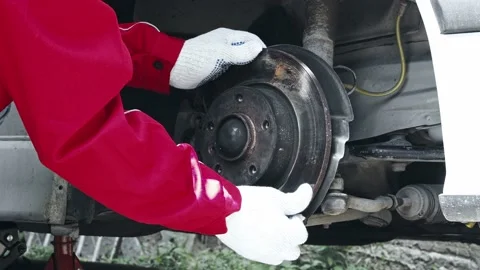A car mechanic checking weared disc brakes, backing plates on a car. Stock Footage 217400719