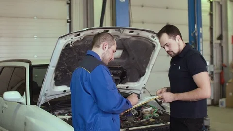 Car mechanic is discussing with client in auto repair service with clipboard Stock Footage 74605520