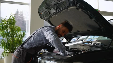 Car mechanic inspecting engine under open hood in workshop with lamp Stock Footage 300613391