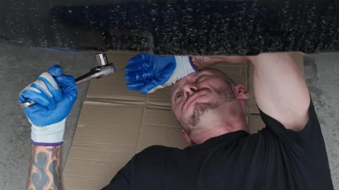 A car mechanic laying down on the ground working underneath a car Stock Footage 246134147