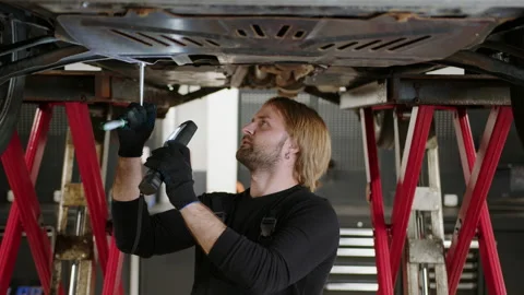 A car mechanic in uniform with a flashlight inspects the bottom of the car Stock Footage 221545935