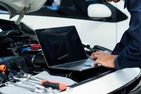 Car mechanic using laptop computer examining tuning fixing repairing car en.. Stock Photos