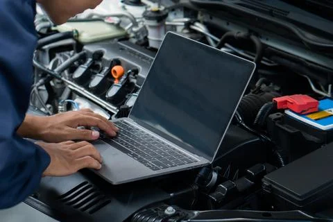Car mechanic using laptop computer examining tuning fixing repairing car en.. Stock Photos