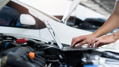 Car mechanic using laptop computer examining tuning fixing repairing car en.. Stock Photos
