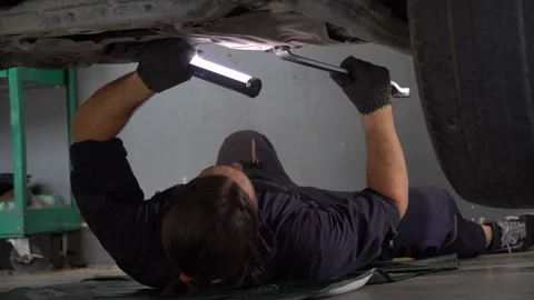 Car mechanic worker lying under car checking and using wrench with torch re.. Stock Footage 246988922