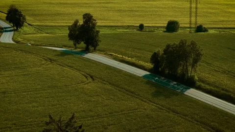 Car moving on winding road between golden fields during sunset. Red hatchback Stock Footage 323594867