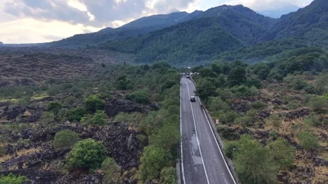Car navigate winding road through green landscape surrounded by volcanic rock 動画素材 345614848