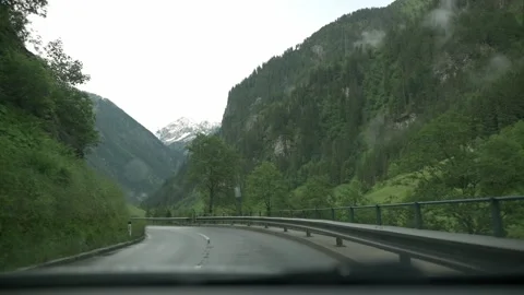 A car navigates a winding road through a lush alpine valley in Austria, with Stock Footage 281615600
