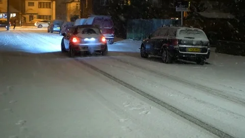 A car is oassing though in snow falling on streets of Epsom, Surrey Stock Footage 103585898