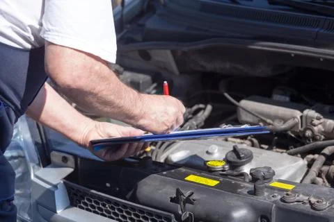 Car or auto mechanic checking a car engine and writing on the clipboard Stock Photos