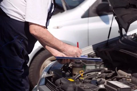 Car or motor mechanic checking a car engine and writing on the clipboard Stock Photos