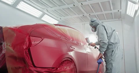 A car painter in a protective suit and mask is spray painting a car in a Stock Footage 276606937