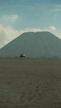 A car is parked on a dirt road in front of a large mountain Stock Photos