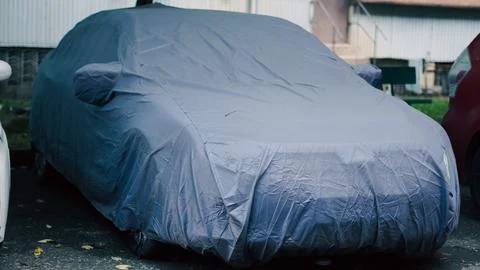 A car is parked outdoors while completely covered by a protective grey fabric Stock Photos