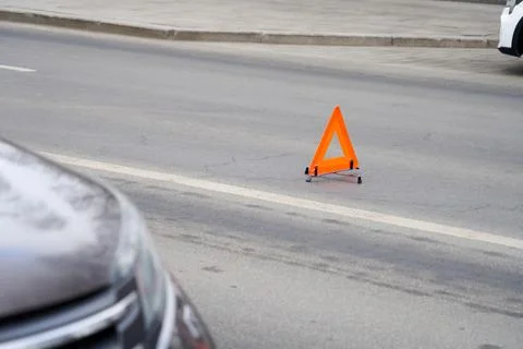 A car is parked on the side of the road with a triangular orange sign in fr.. Stock Photos