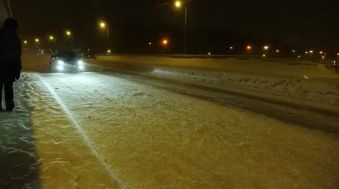 Car passing by a commuter waiting at a bus stop one snowy night Stock Footage 12714028