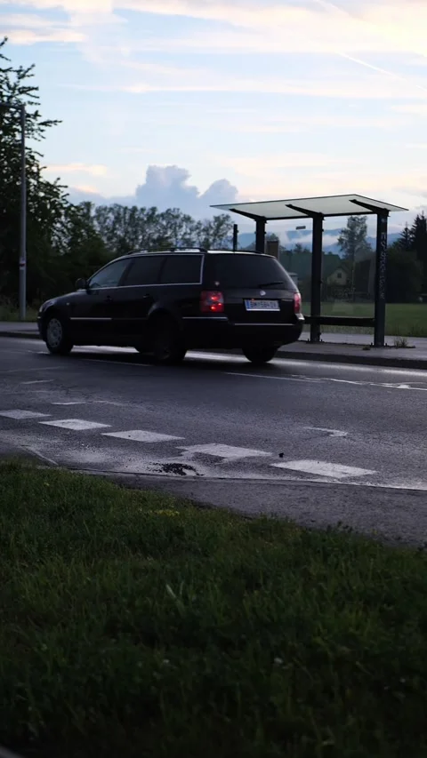 Car passing an empty rural bus stop on a countryside road at dusk 動画素材 343566071