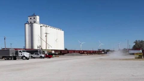 Car passing a Kansas grain elevator with distant rotating wind turbines Stock Footage 347405168
