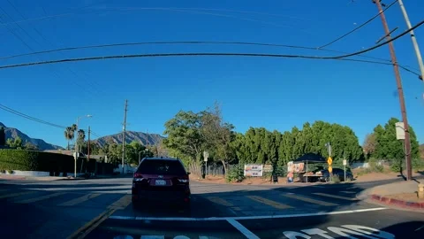 Car point of view of an intersection past green hillsides, LA Stock Footage 343475505