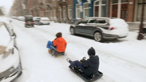 Car pulling kids on a sled during snowfall. Amsterdam, Netherlands. Stock Footage 148080088