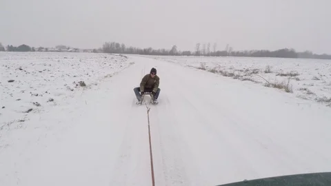 Car pulling man on the sled on snowy road Stock Footage 106106181