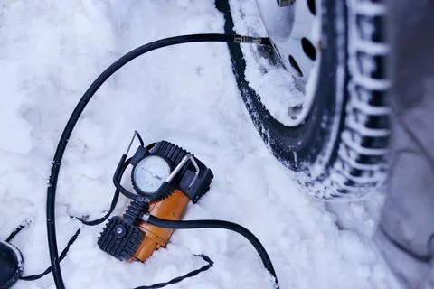 Car pump compressor pumps up a flat tire of a car in winter on a snowy path i Foto stock