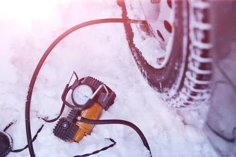 Car pump compressor pumps up a flat tire of a car in winter on a snowy path i Stock Photos