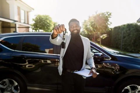 Car Rental Service. Happy African Man salesmanager or client Holding Key And Stock Photos
