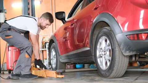 Car repair workshop. The young master takes out the lift from under the car Stock-Footage 212343367