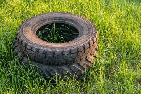 Car rubber tires thrown into a stack on green grass. Environmental pollution. Stock Photos