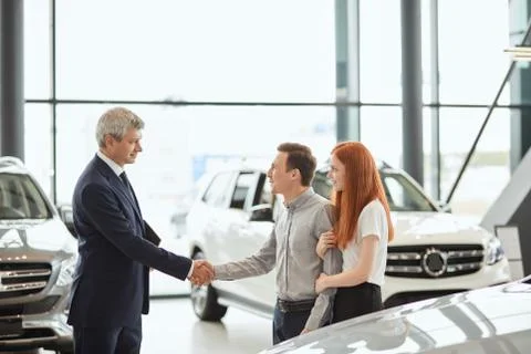 Car sales manager telling about the features of the car to the customers at the Stock Illustration