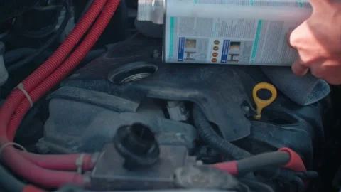 Car service. A man pours engine oil into a car engine from a tin can. Daytime Stock Footage 160991653
