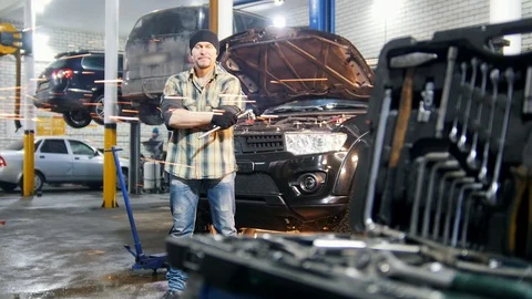 Car service. Mechanic man standing by the car holding a tool and looking in the Stock Footage 101689202