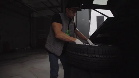 Car serviceman pulls the wheel out of the trunk and sets for washing. 60 FPS Stock Footage 93026240