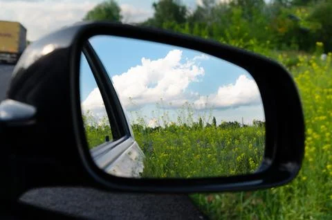 Car side mirror reflecting bright green field and sky. Stock Photos