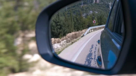 Car side mirror reflecting mountain road during a scenic drive Stock Footage 345063476
