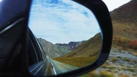 Car side mirror reflects scenic mountain road with clear blue sky Stockbeeldmateriaal 342734390