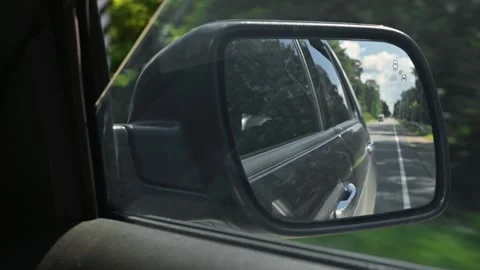 A car side mirror shows a view of a road lined with trees. The mirror captures Stock Footage 345868730