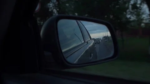 Car side mirror view reflecting road and cloudy sky at dusk Stock Footage 336177925
